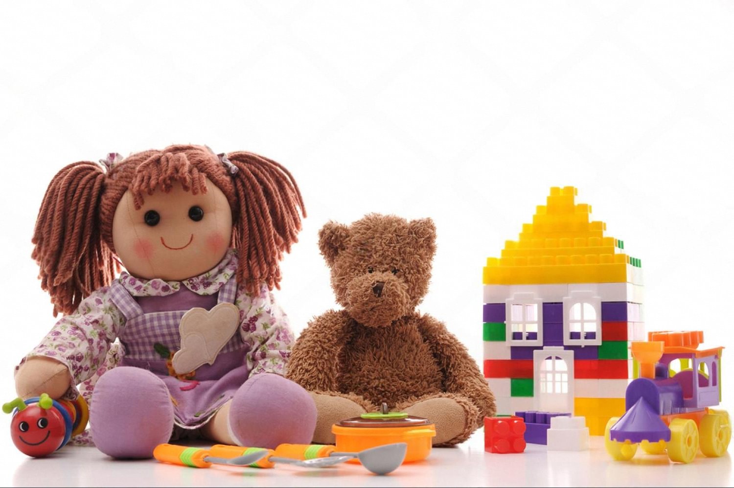 A collection of children's toys including building blocks, a doll, a teddy bear and a toy train arranged together