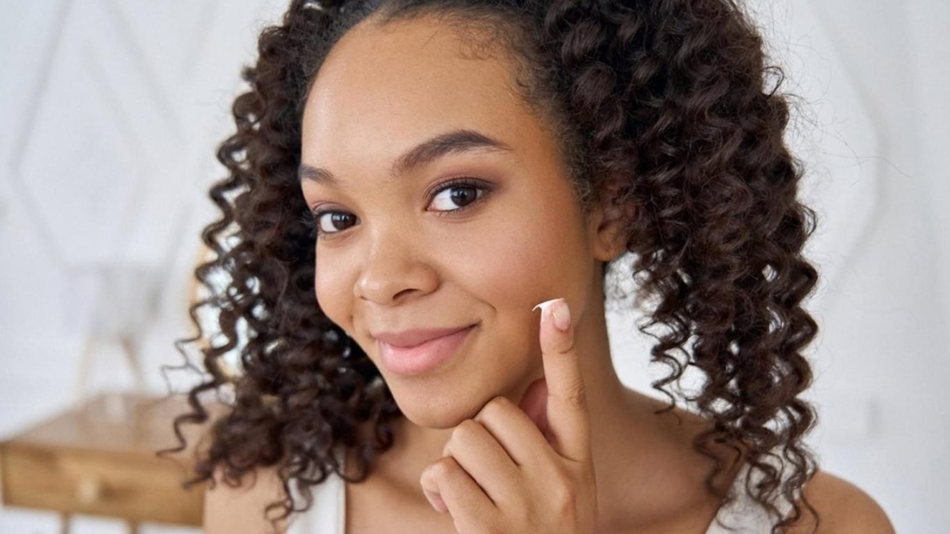 Young woman applying moisturizer to her cheek as part of a Dubai skincare routine